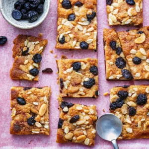 Blueberry Cottage Cheese Bake – Soft baked squares topped with juicy blueberries and crunchy nuts on a pink parchment background.