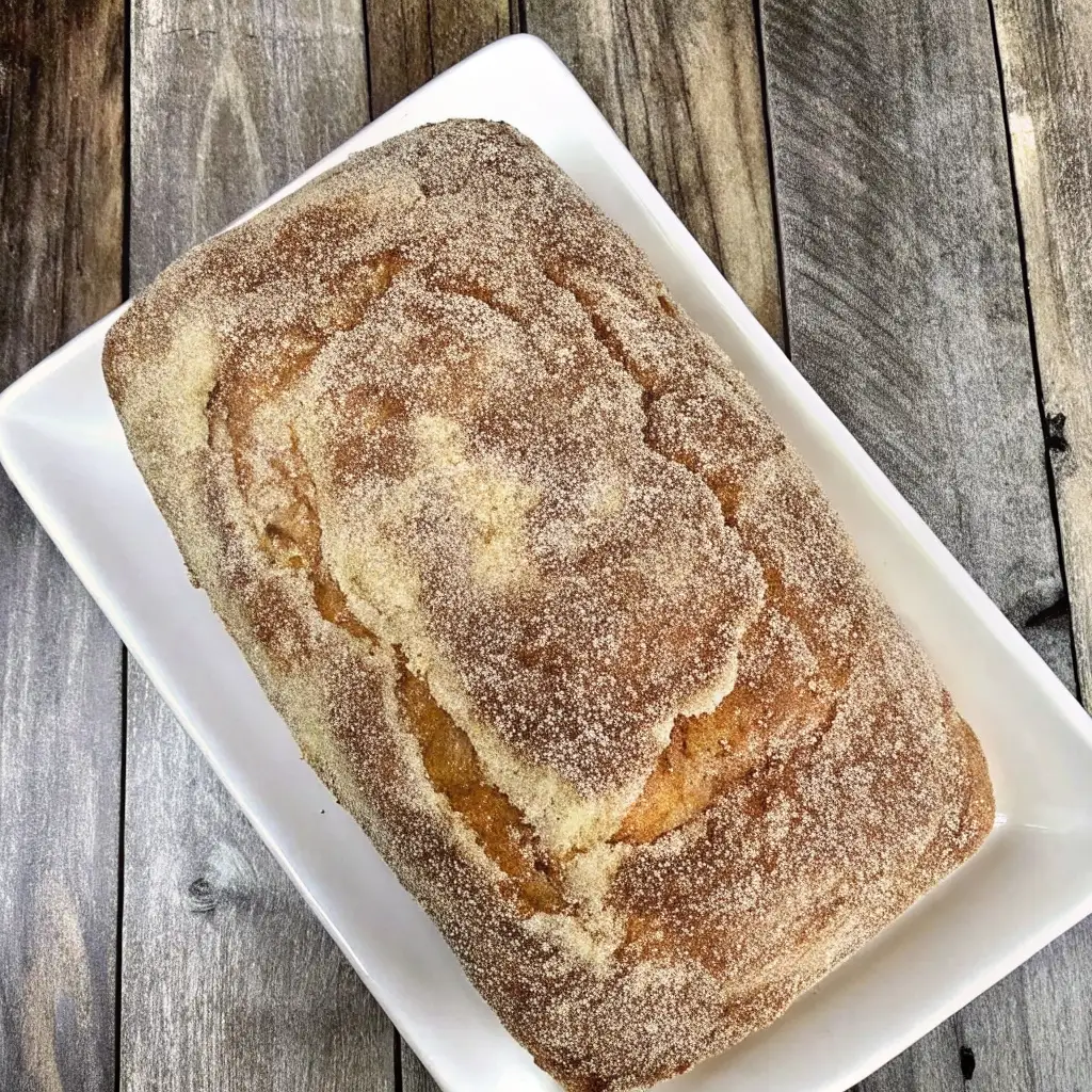 Cinnamon Donut Bread – Golden loaf coated in cinnamon sugar, served on a white platter over rustic wooden background.