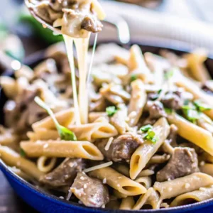 Steaming bowl of philly cheesesteak pasta with melted cheese on top